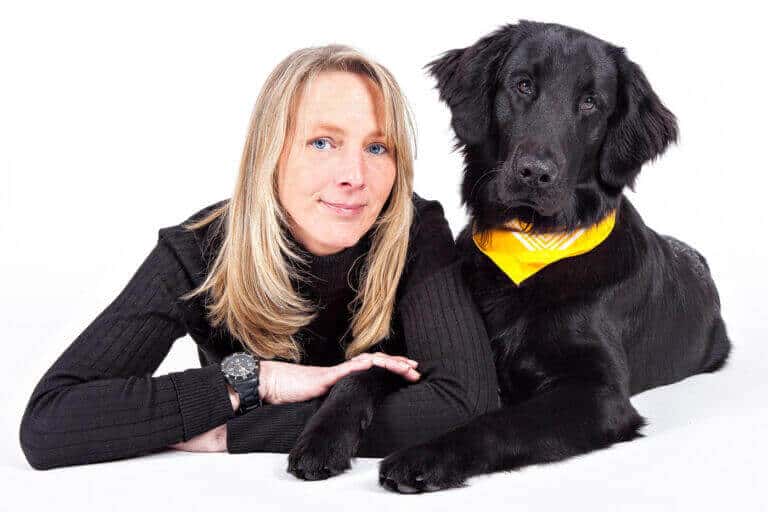 Blonde Frau liegt im Fotostudio neben ihrem schwarzen Hund mit gelbem Halstuch
