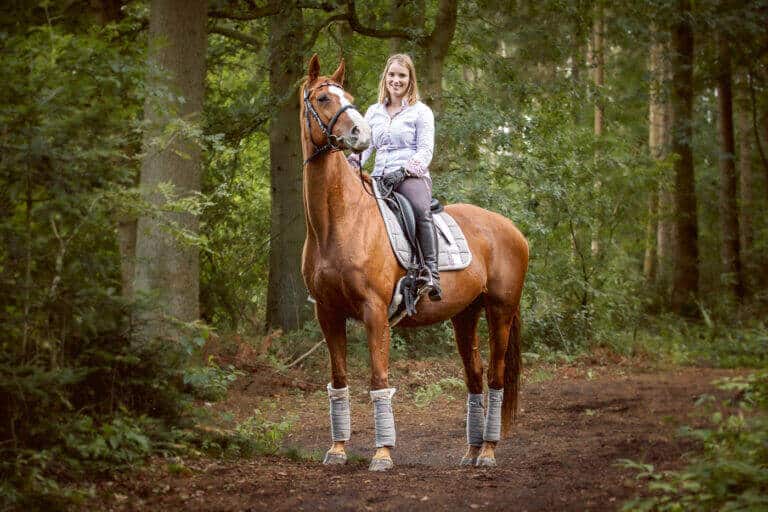 Junge Frau reitet auf einem hellen Pferd über einen Waldweg