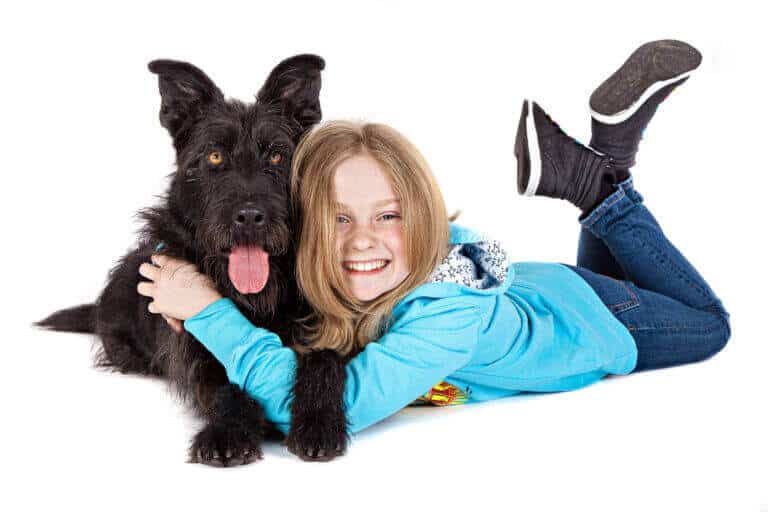 Lachendes Mädchen liegt im Fotostudio neben einem schwarzen Terrier