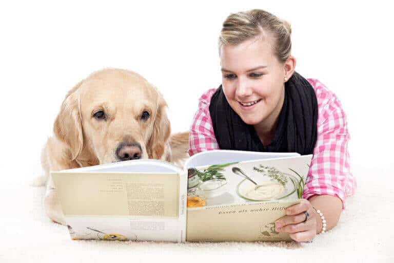 Junge Frau blättert in einem Buch, neben ihr liegt ein Golden Retriever